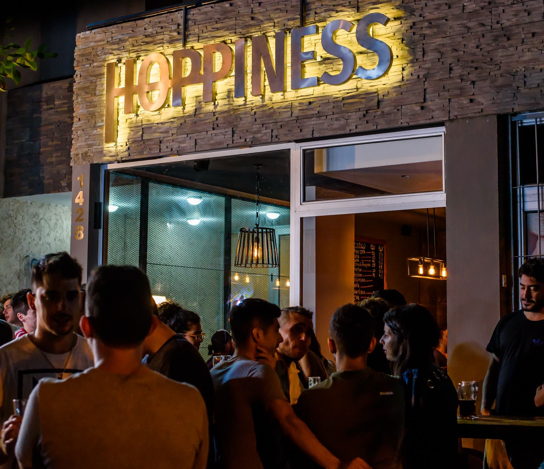 Fachada del primer Hoppiness Club de Cervezas en General Paz 1428, Cofico, durante una noche con el local lleno.