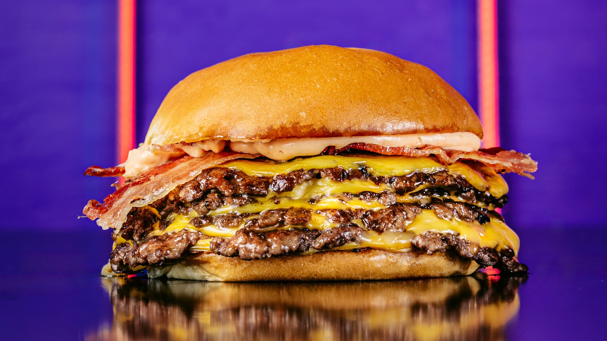 Hamburguesa Ultra Bacon de Hoppiness Club: cuatro porciones Ultrasmash, cheddar, bacon y salsa Hoppiness, sobre fondo azul