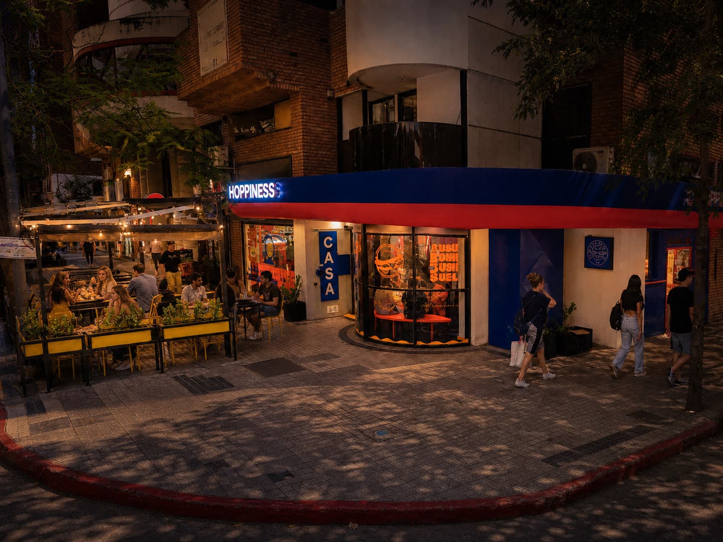 Fachada nocturna de Hoppiness Club Nueva Córdoba en Estrada y Buenos Aires, con clientes en la terraza y la marquesina azul y roja iluminada.