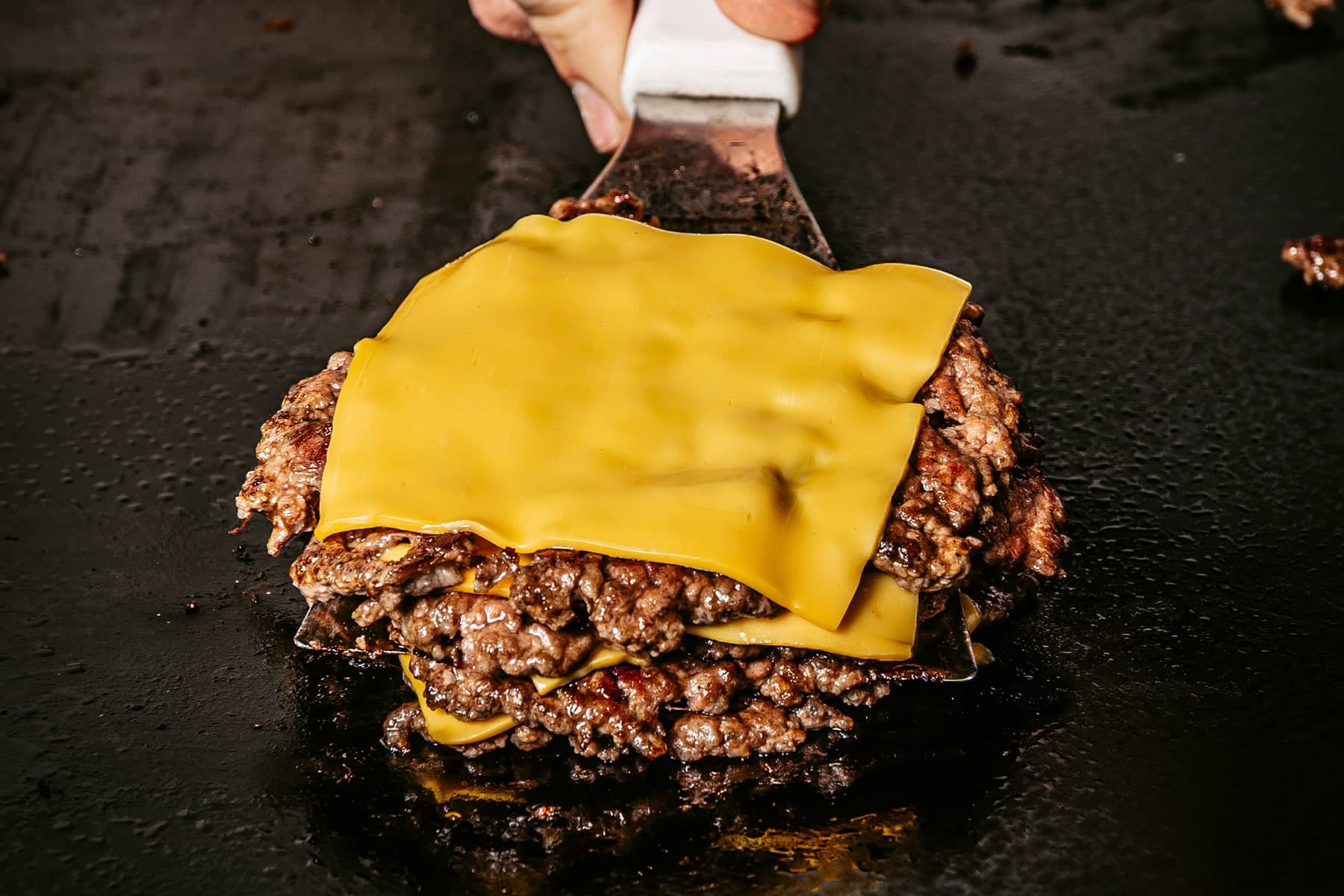 Cuatro porciones Ultrasmash con cheddar, levantadas de la plancha con una espátula.